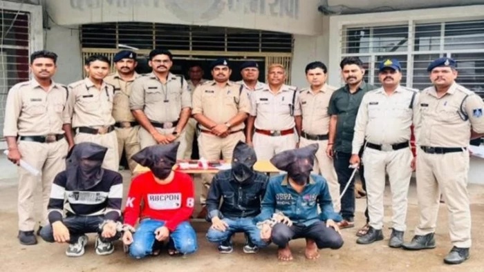 Group of uniformed police officers standing behind four kneeling suspects with hoods covering their faces, posing for a photo during an arrest operation.