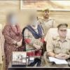 Police officer seated at a desk with papers; several officers and civilians stand behind, faces blurred, in a police station setting with a trophy on the desk.