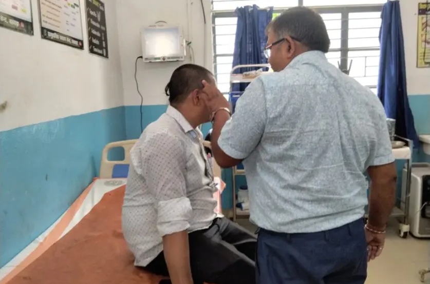 Male patient sits on a hospital bed while a clinician checks his ear in a hospital room with blue walls and equipment nearby.
