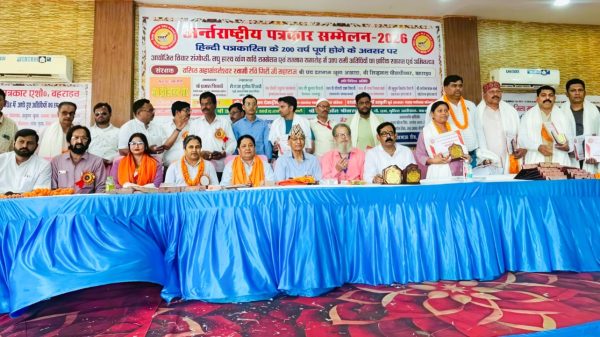 Dignitaries seated at a long blue-draped table on stage during a Hindi conference, with awards and a banner behind them.