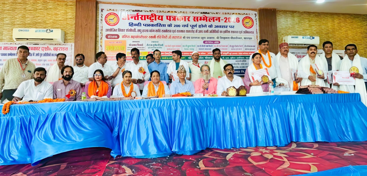 Dignitaries seated at a long blue-draped table on stage during a Hindi conference, with awards and a banner behind them.