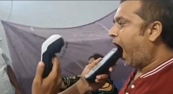 Man with his mouth open as a tester places a handheld device near his lips, with another device in the tester's other hand.