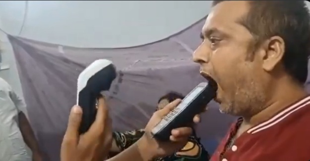 Man with his mouth open as a tester places a handheld device near his lips, with another device in the tester's other hand.