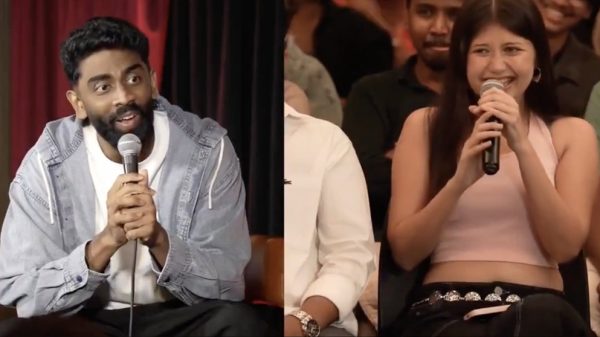 Two people sit side by side on a stage, each holding a microphone and speaking to an audience.