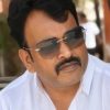 Portrait of a man with a mustache wearing sunglasses and a white shirt, outdoors with a blurred background.