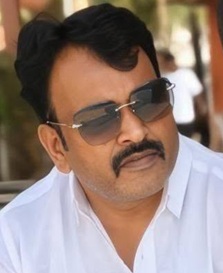 Portrait of a man with a mustache wearing sunglasses and a white shirt, outdoors with a blurred background.