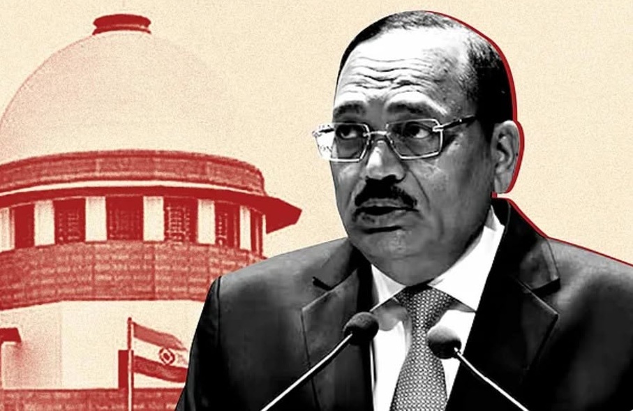 A suited man with glasses speaks into two microphones at a formal event, with a red-tinted government building backdrop behind him.