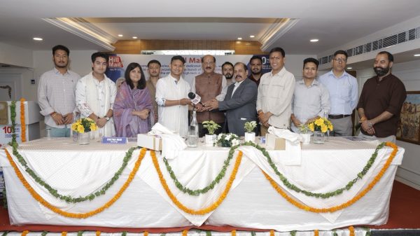 Group of people standing behind a long, decorated table at a formal press event, hands joined in a handshake.