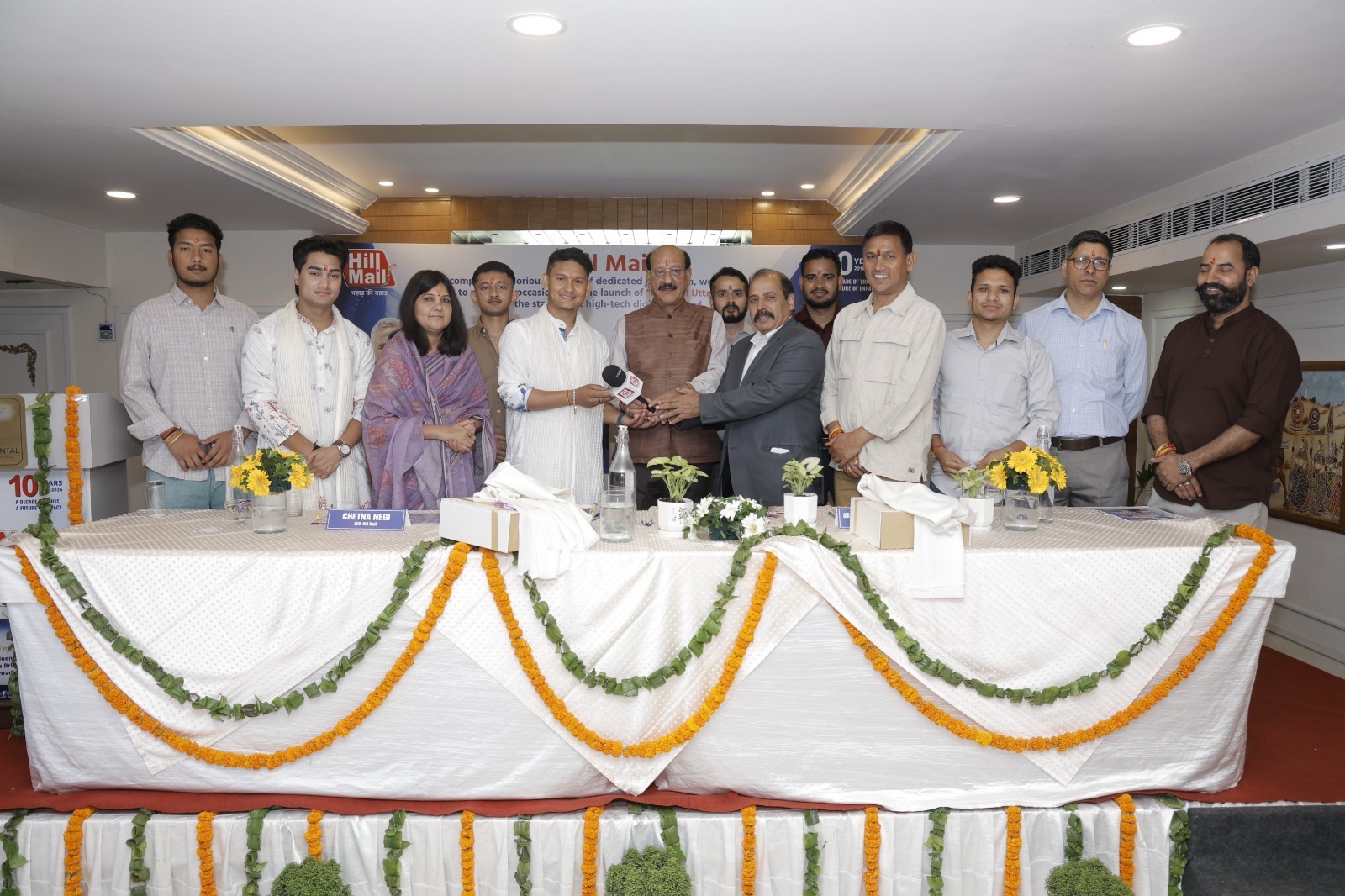 Group of people standing behind a long, decorated table at a formal press event, hands joined in a handshake.