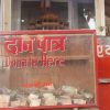 Red donation box with a transparent front showing cash inside; sign reads 'Donate Here' in English and Hindi.