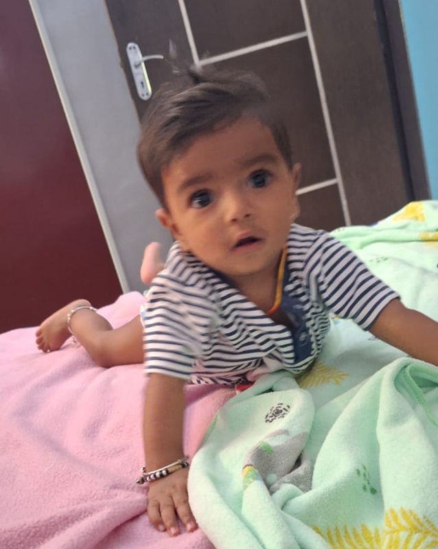 Young child crawling on a bed, looking toward the camera, on pink and green blankets.