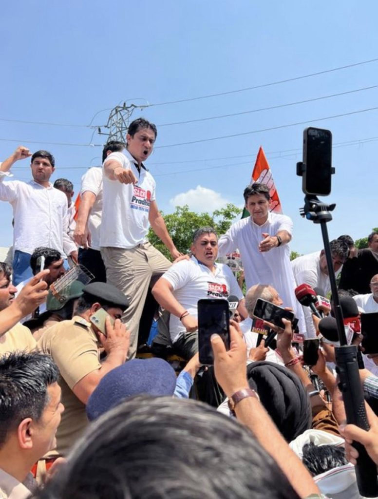Screenshot | No. 1 Indian Media News Portal A man on a pickup truck shouts to a shouting crowd while reporters film with phones and microphones nearby, during a protest.