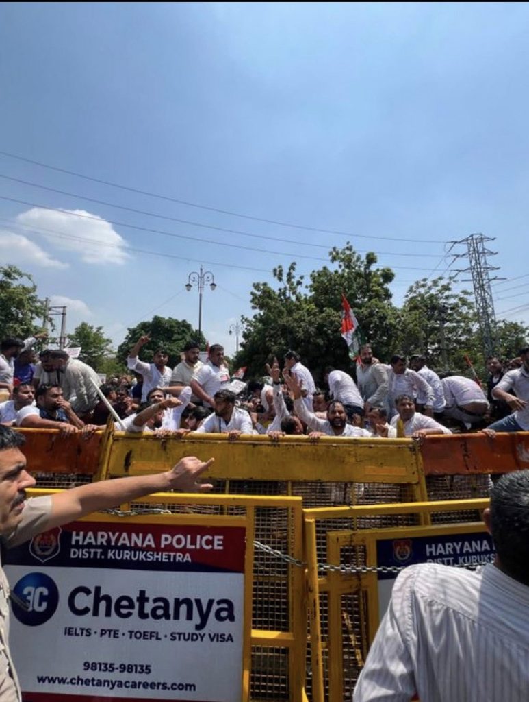 Screenshot | No. 1 Indian Media News Portal Large crowd of men behind yellow barricades, some raising hands, with a Haryana Police banner and a Chetanya Careers sign visible.