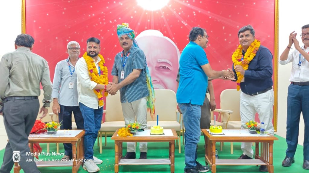 ifwj_2 | No. 1 Indian Media News Portal Group of men on a stage exchanging handshakes, wearing marigold garlands, with a red decorative backdrop and small cakes on tables in front.