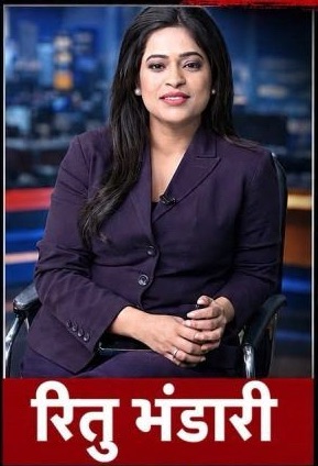 TV news anchor seated in a studio wearing a purple suit, with a red lower-third banner showing white Hindi text.
