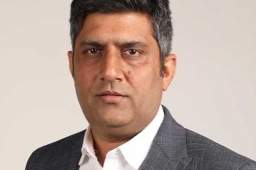 Portrait of a man in a gray suit and white shirt looking at the camera against a neutral background.