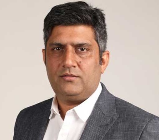 Portrait of a man in a gray suit and white shirt looking at the camera against a neutral background.