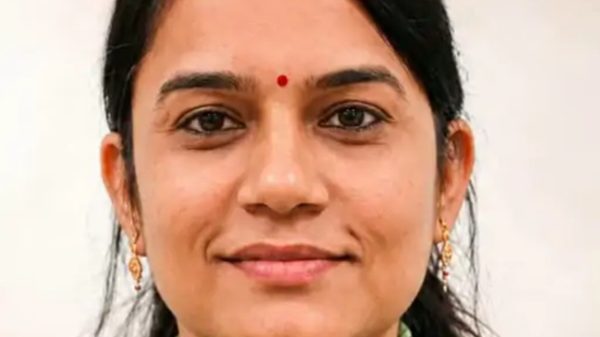 Close-up portrait of a smiling woman with a red bindi, wearing gold earrings.
