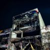 Nighttime view of a fire-damaged, scaffolding-covered building with a charred facade and yellow caution tape surrounding the site.