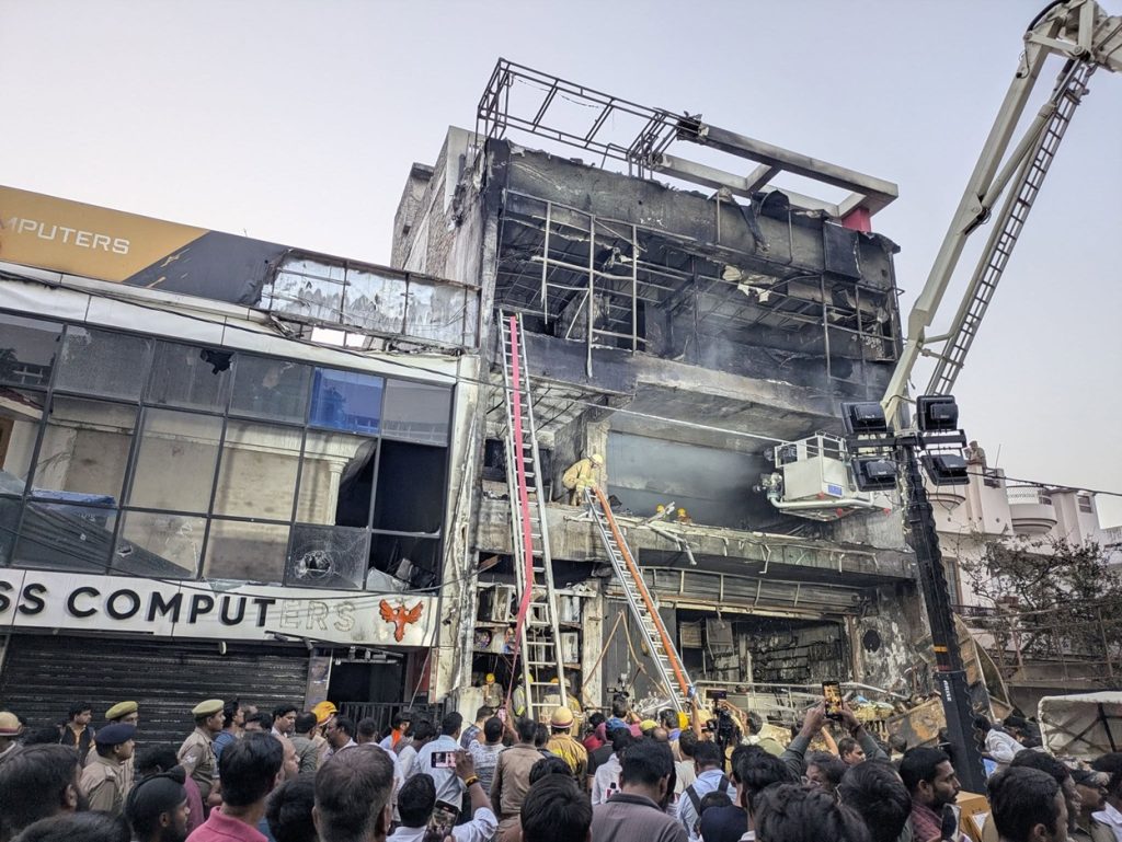 lko coaching | No. 1 Indian Media News Portal Crowd gathers as firefighters work at a partially collapsed multi-story building, with a crane and rescue ladders in use.