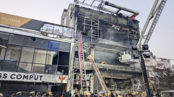 Crowd gathers as firefighters work at a partially collapsed multi-story building, with a crane and rescue ladders in use.
