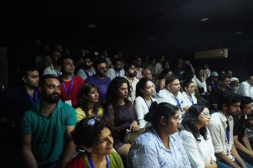 mahesh_bhatt | No. 1 Indian Media News Portal Crowd of people seated and standing in a dimly lit auditorium, many wearing blue lanyards at a conference or event.
