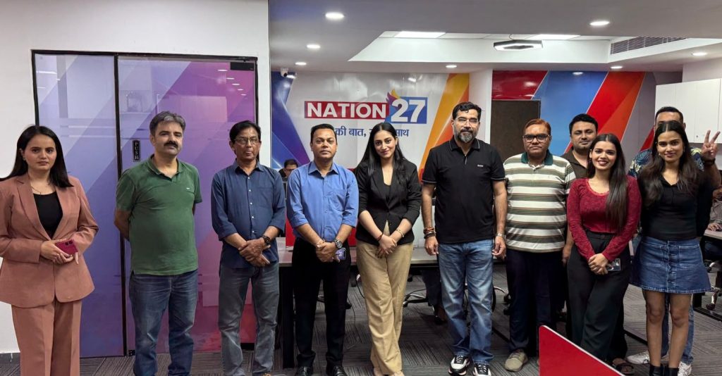 Group of eleven staff members posing in a newsroom with a Nation27 banner in the background.