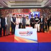 Group of formally dressed people standing on a stage behind a podium with 'NATION 27' branding and sparkly backdrop.