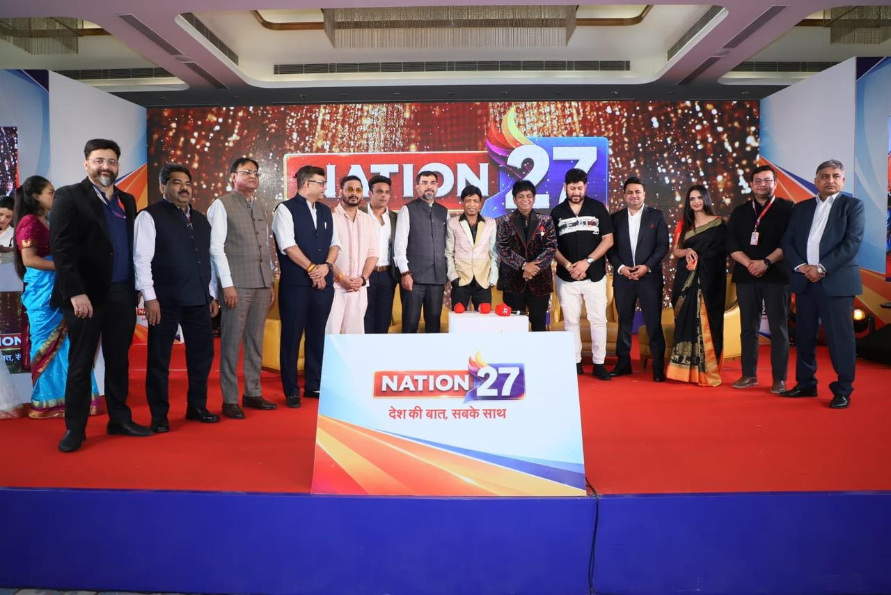 Group of formally dressed people standing on a stage behind a podium with 'NATION 27' branding and sparkly backdrop.