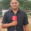 A male reporter in a black shirt holds a microphone labeled 'ZEE MEDIA' outdoors with trees in the background.