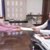 Two men exchange a document across a large desk in a formal office, with an ANI watermark in the corner.
