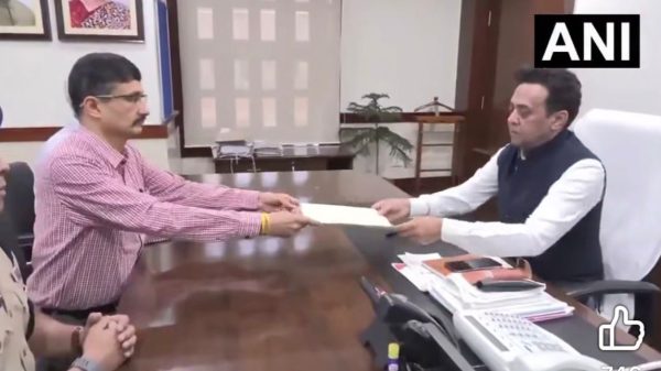 Two men exchange a document across a large desk in a formal office, with an ANI watermark in the corner.