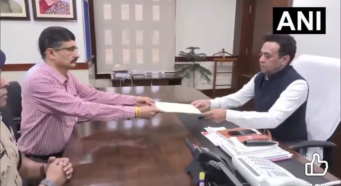 Two men exchange a document across a large desk in a formal office, with an ANI watermark in the corner.