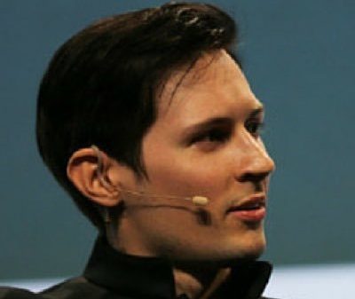 Side profile of a man with a headset microphone speaking at an event.