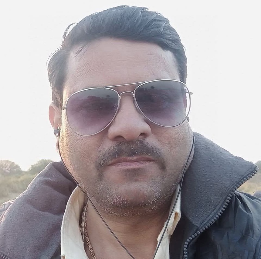 prabuddha | No. 1 Indian Media News Portal Man wearing aviator sunglasses and a dark jacket, outdoor portrait with earphones visible and a wiry mustache.