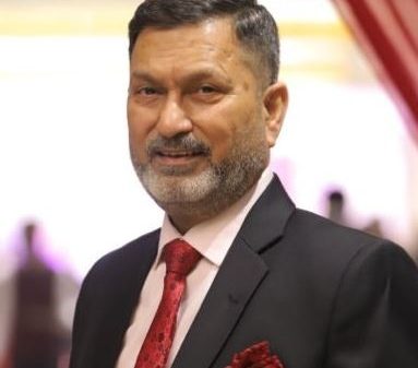 Man in a black suit and red tie posing at a formal event, with a pocket square visible.