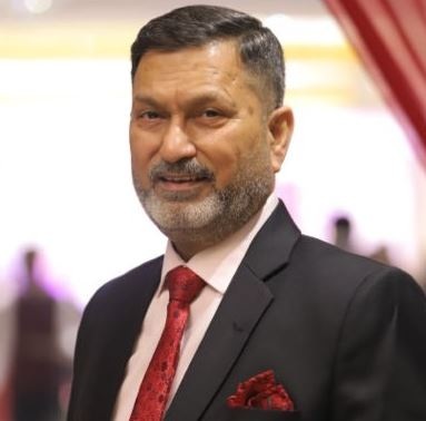 Man in a black suit and red tie posing at a formal event, with a pocket square visible.