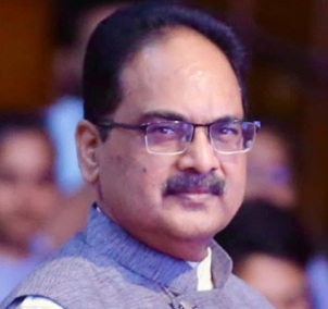 Portrait of a man with glasses and a mustache, wearing a light blue shirt, looking toward the camera in a crowd.