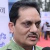 Close-up of a man in a green kurta speaking into microphones at an outdoor event with banners in the background