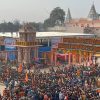 Huge crowd gathered at a temple complex during a festival, with orange flags, colorful banners, and ornate stone arches framing the entrance.