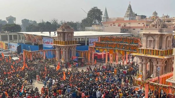 Huge crowd gathered at a temple complex during a festival, with orange flags, colorful banners, and ornate stone arches framing the entrance.