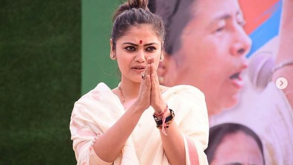 Young Indian woman in a white sari with hands pressed together in a namaste gesture outdoors