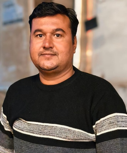 sanjay_parik | No. 1 Indian Media News Portal Portrait of a man in a black sweater with light gray stripes, standing indoors and facing the camera.