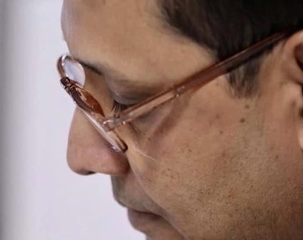 Close-up side profile of a man wearing brown-rimmed glasses looking downward.