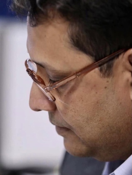 Close-up side profile of a man wearing brown-rimmed glasses looking downward.