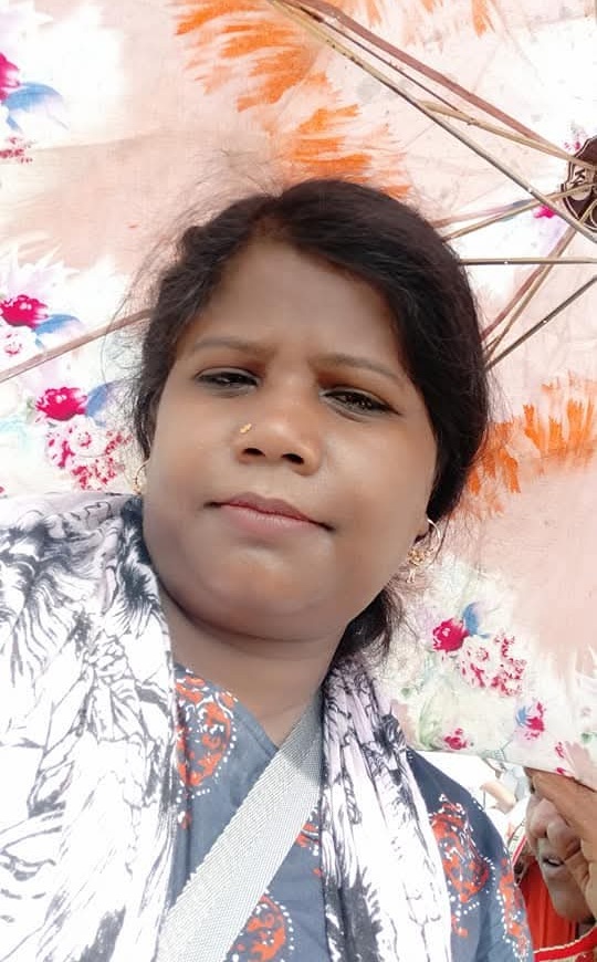 Close-up portrait of a woman outdoors, with a floral umbrella behind her and a colorful backdrop behind her head.
