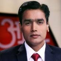 Professional headshot of a man in a dark suit and red tie, facing the camera against a blurred background.