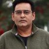 Portrait of a man wearing glasses and a green zip-up jacket outdoors.