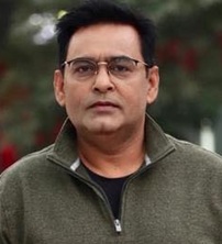 Portrait of a man wearing glasses and a green zip-up jacket outdoors.