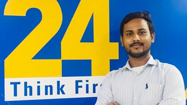 Man with folded arms posing in front of a blue wall that shows a 'News 24' sign and 'Think First' text behind him.